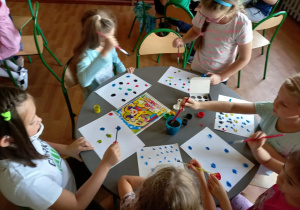 Dzieci siedzą przy stoliku i malują kolorowe plamy.